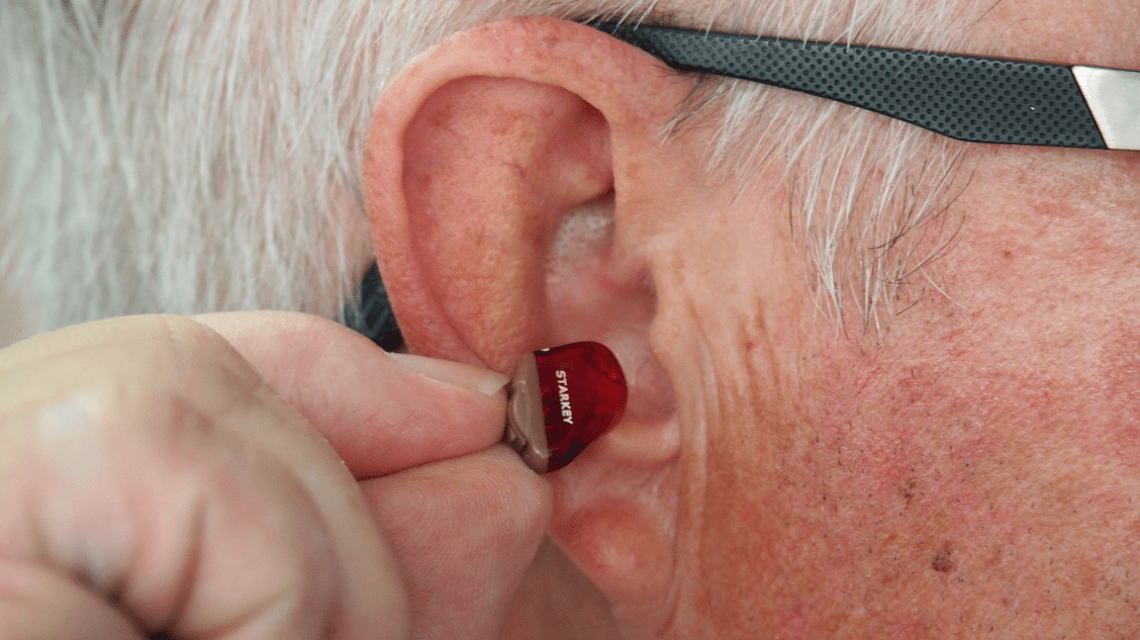 Man inserting a hearing aid after cleaning his ear to help prevent ear wax build up
