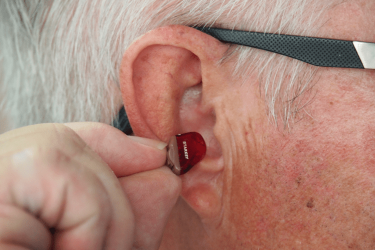 Man inserting a hearing aid after cleaning his ear to help prevent ear wax build up
